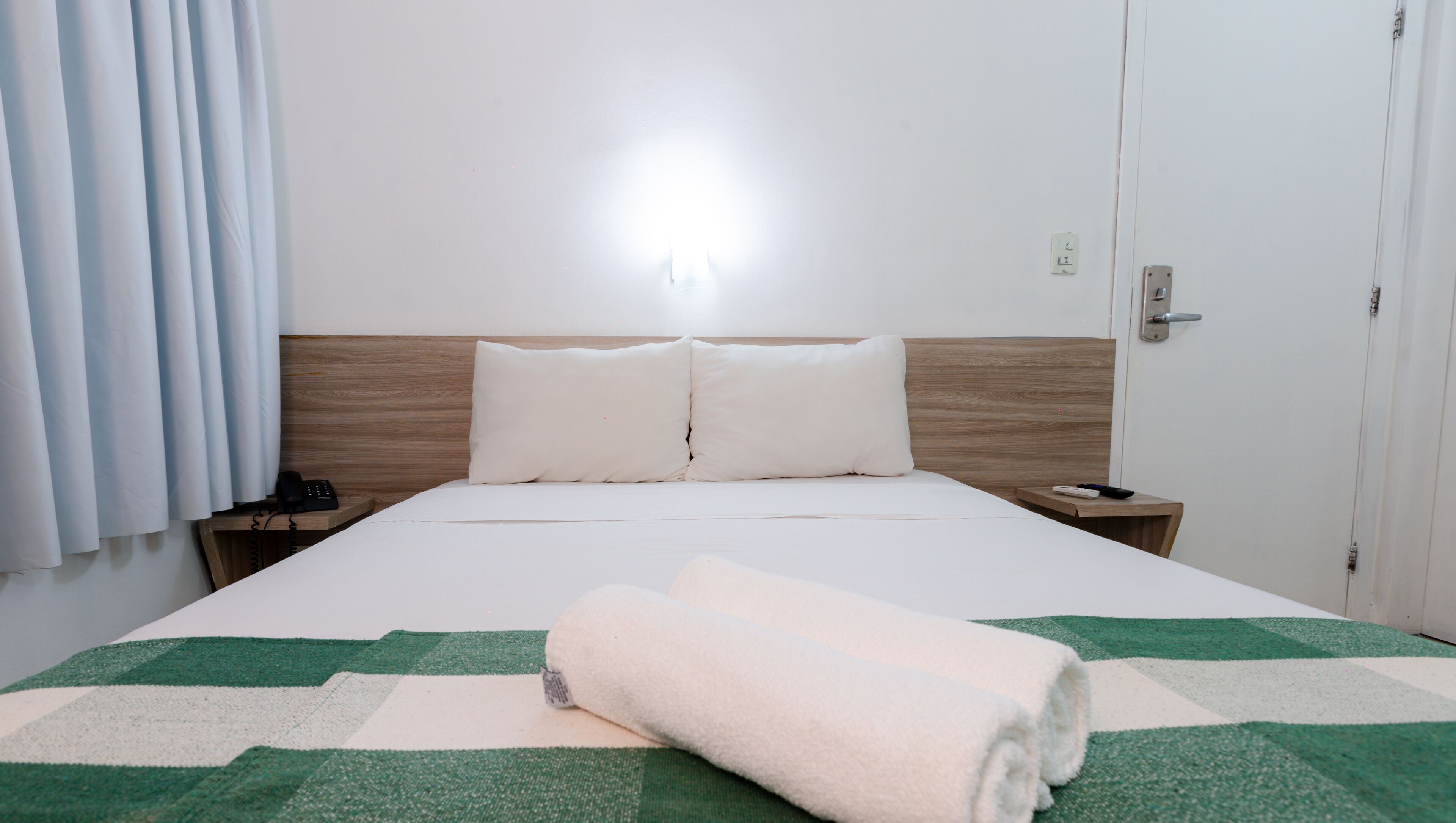 A hotel room with a bed, a nightstand, a telephone, and a door.