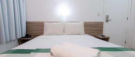 Una habitación de hotel con cama, mesita de noche, teléfono y puerta.