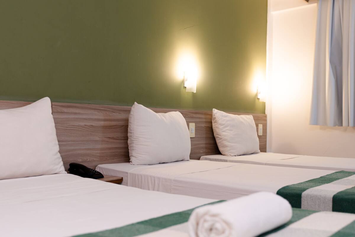 Habitación de hotel con dos camas, cada una con ropa blanca y una almohada a rayas verdes. Hay luces empotradas en la pared y un teléfono en la mesita de noche.
