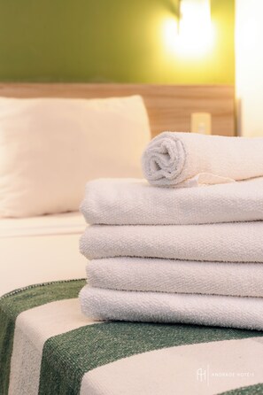 Un montón de toallas blancas sobre una cama con una colcha de cuadros verdes y blancos.