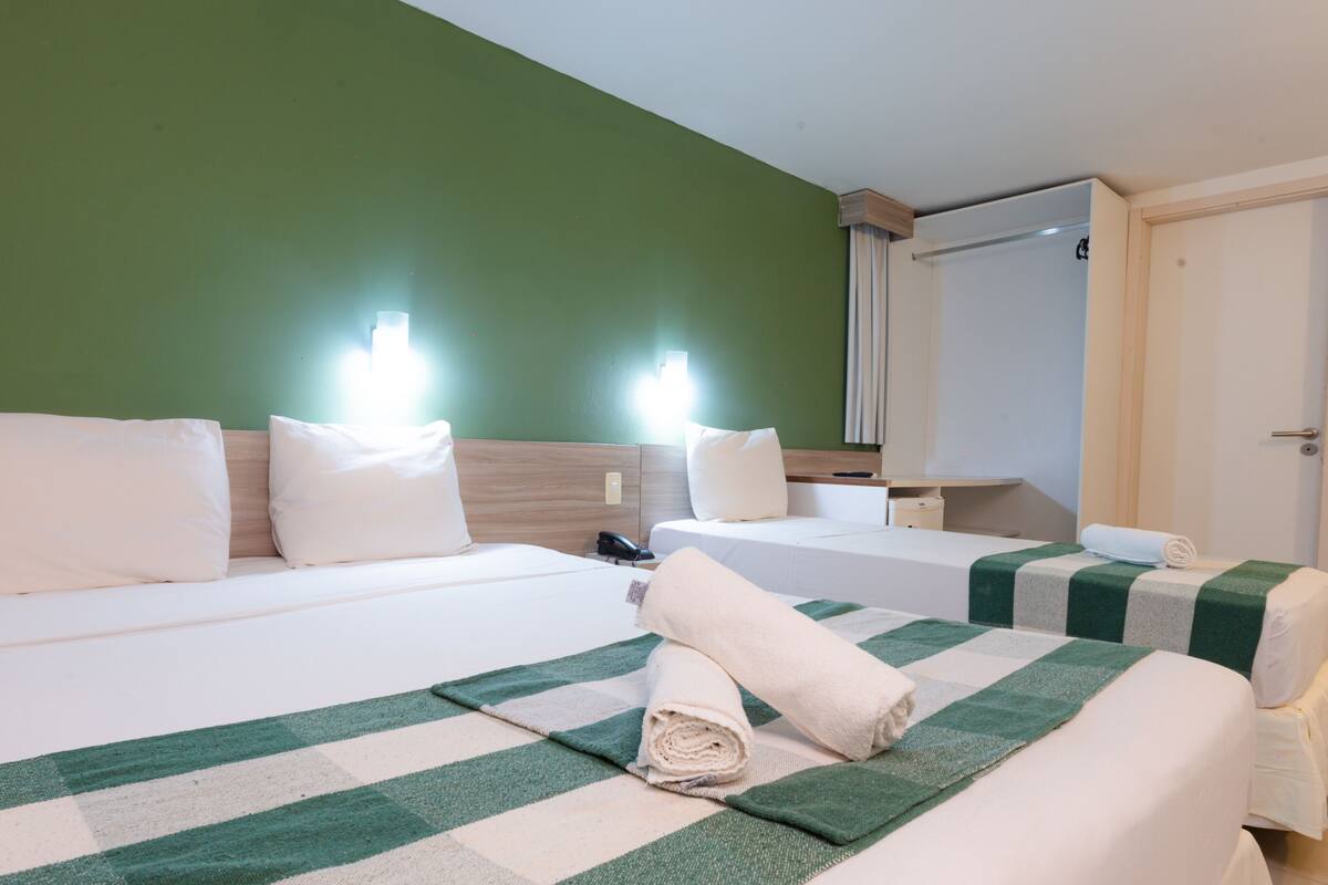 Habitación de hotel con dos camas, una pared verde, cabecera de madera y un espejo.
