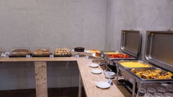 Buffet com diversos alimentos, incluindo pães, bolos e frutas.