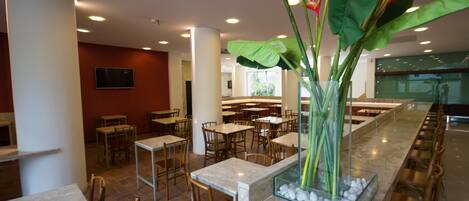 A modern restaurant with marble counters, wooden chairs, and a central decorative plant.