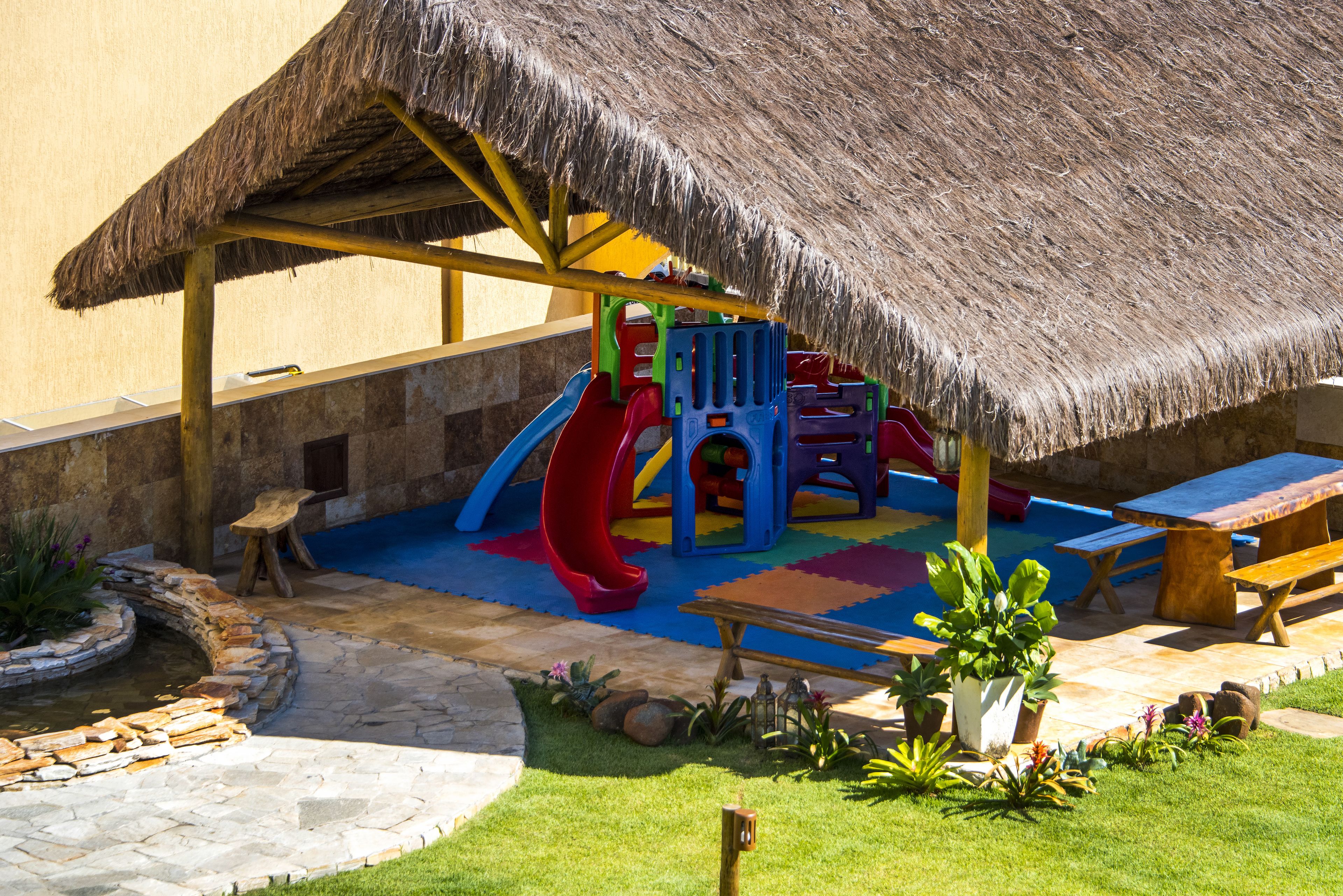 A play area with a thatched roof, colorful play structures, and a small pool.