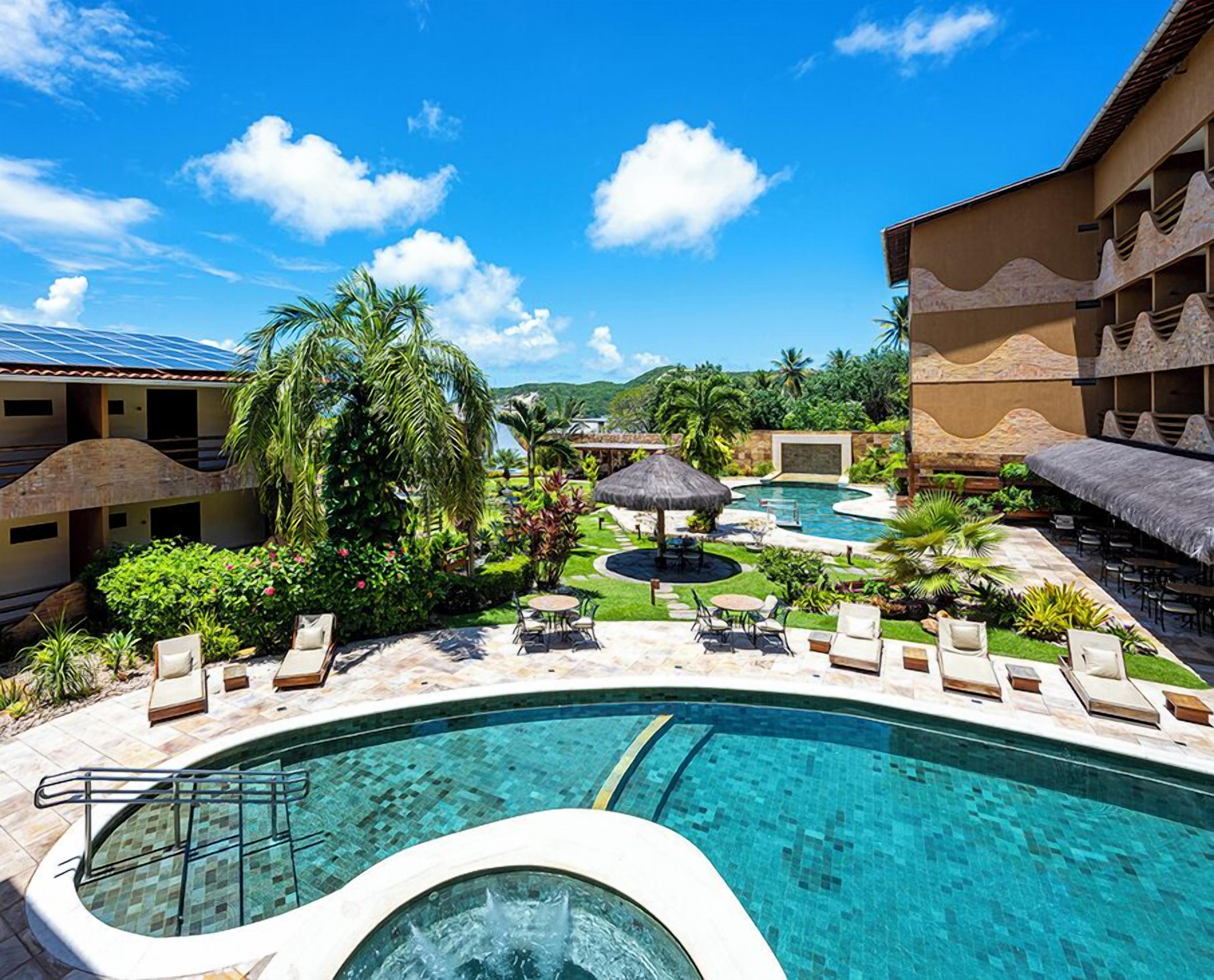 Resort com uma grande piscina externa, áreas de estar e paisagismo tropical.