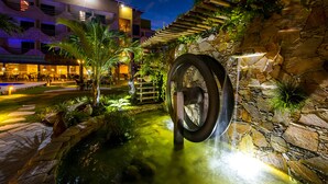 A nighttime outdoor area with a water feature, stone walls, and a building with multiple floors and balconies. - Natal Dunnas Hotel (Natal)