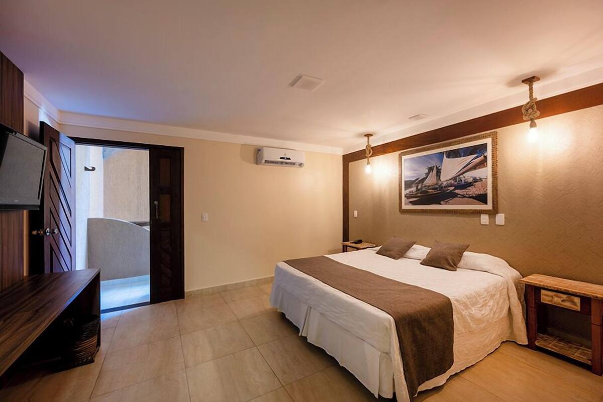 Ein Hotelzimmer mit Bett, Nachttischen, einem Fernseher, einem Bild an der Wand und einer Tür zu einem anderen Raum.
