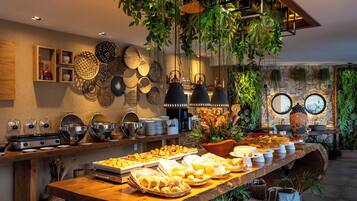 A buffet setup with various food items, a wooden table, hanging plants, and decorative plates on the wall.