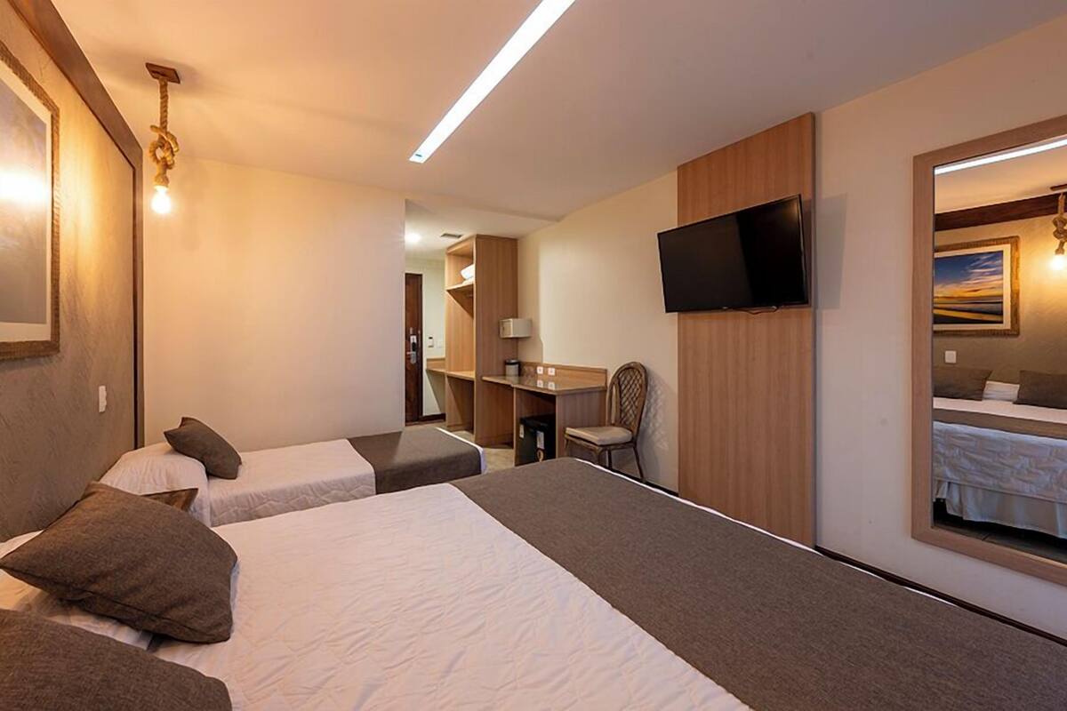 Ein Hotelzimmer mit zwei Betten, einem Schreibtisch, einem Stuhl, einem Fernseher und einem Spiegel.