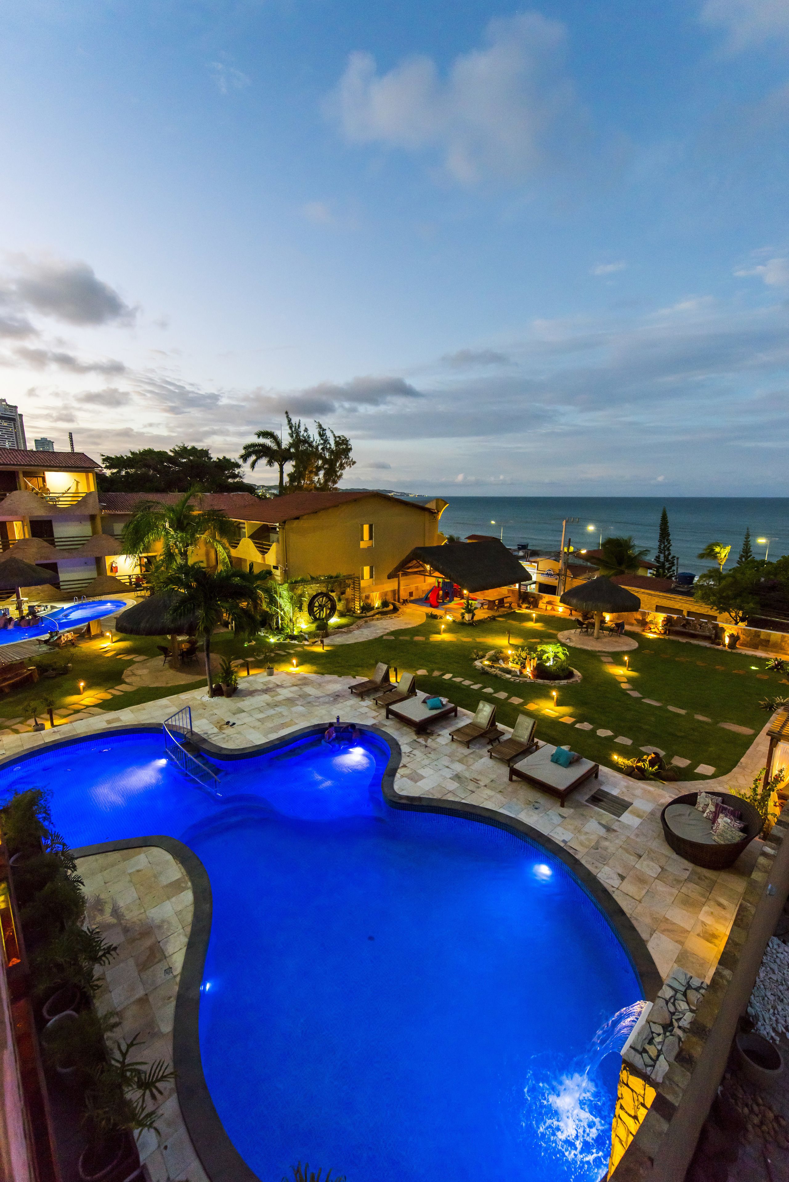 A swimming pool with a curved design, surrounded by lounge chairs and a well-lit patio area.