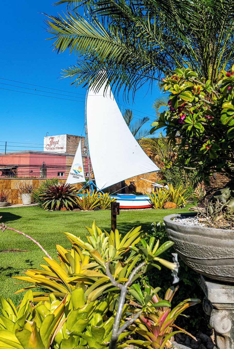 A garden area with a sailboat, a palm tree, and a building with a sign that reads "Nasa Dunes Hotel".