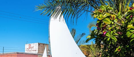 A garden area with a sailboat, a palm tree, and a building with a sign that reads "Nasa Dunes Hotel".