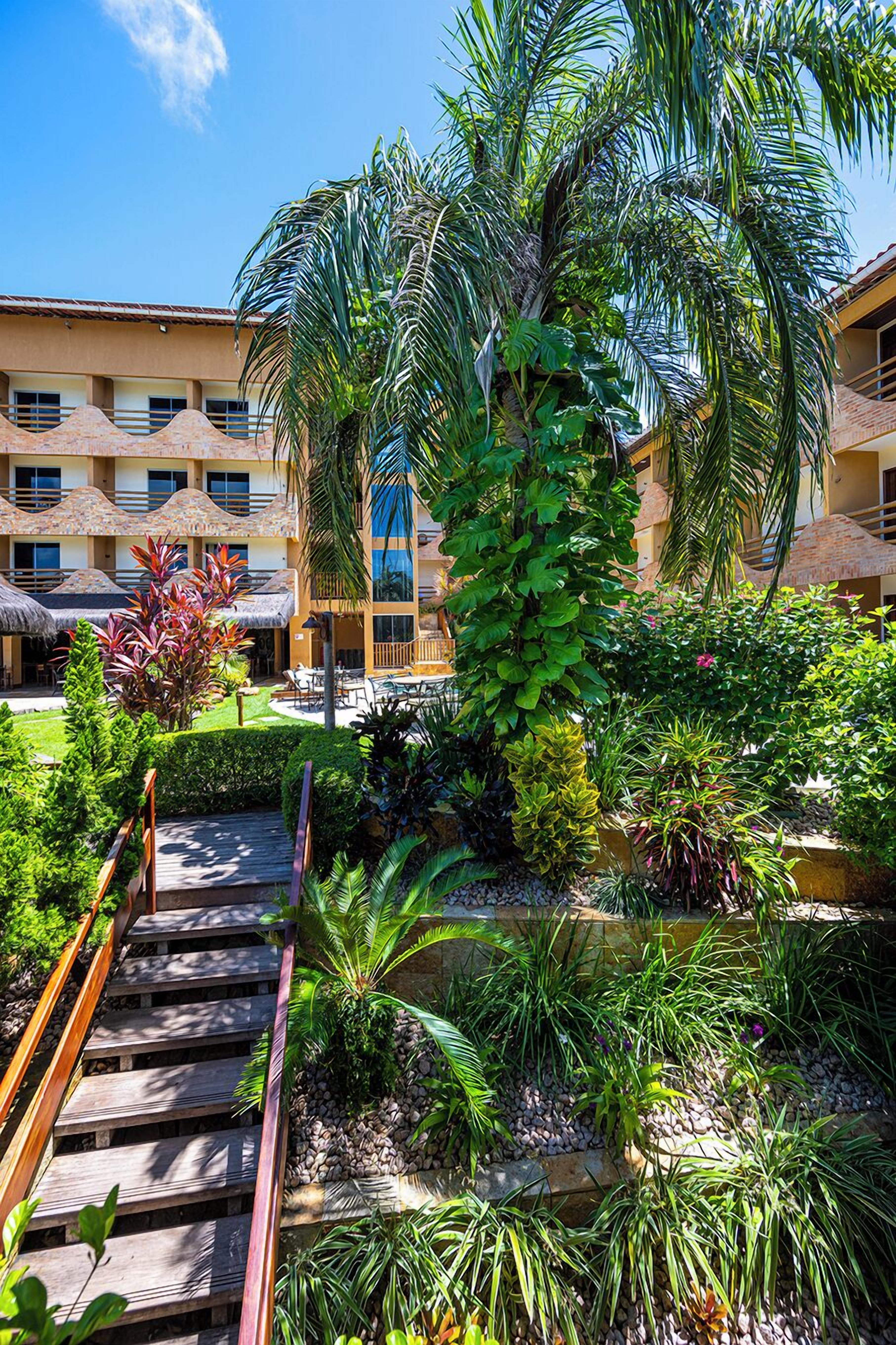 Un hotel con area piscina, circondato da vegetazione lussureggiante e palme.