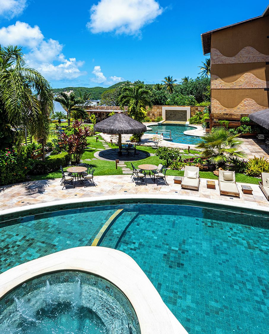A swimming pool with a hot tub, surrounded by lounge chairs and a thatched umbrella.