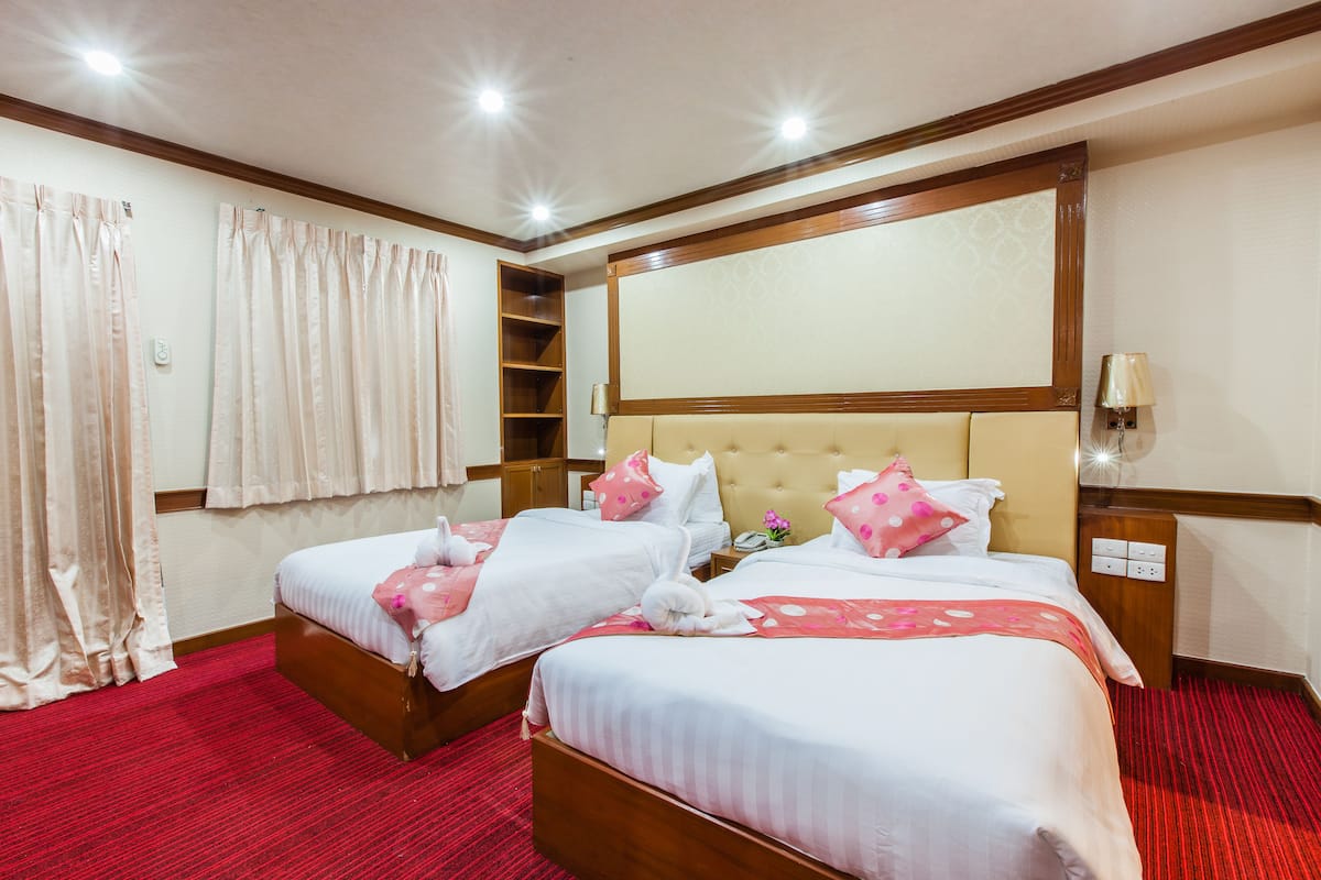 Hotelkamer met twee bedden, een rood tapijt, een houten hoofdbord, een spiegel, een nachtkastje en een lamp.
