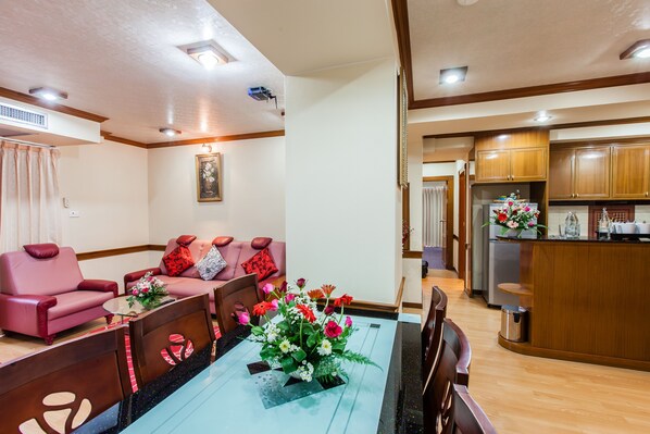 Un salon moderne avec un coin repas, comprenant une table à manger en bois, des canapés roses et une cuisine avec des meubles en bois.