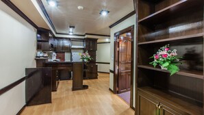 A hallway with wooden flooring, dark wooden cabinets, and a shelf with flowers.