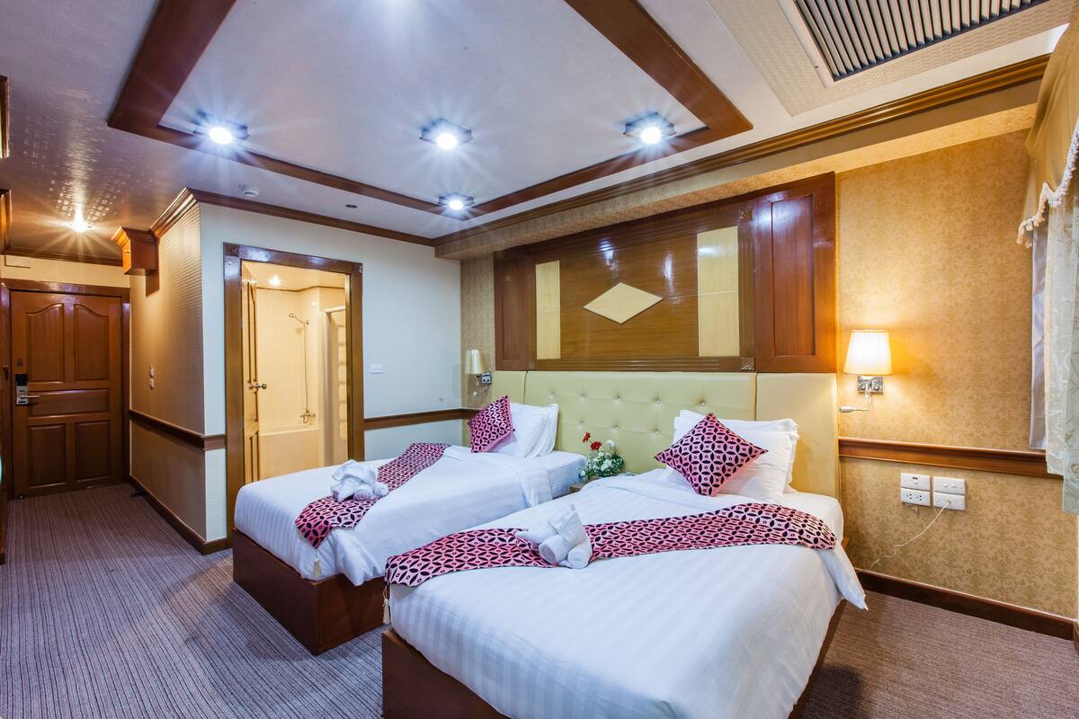 Een hotelkamer met twee bedden, een houten garderobe, een spiegel en een wandlamp.