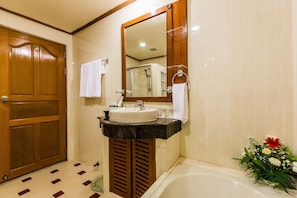 A bathroom with a wooden door, a sink with a mirror above it, a bathtub, and a flower arrangement.