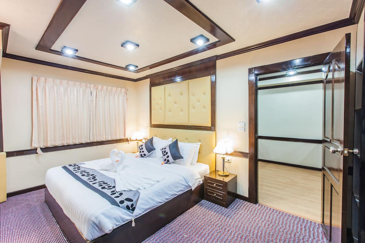 Een hotelkamer met een groot bed, nachtkastjes met lampen, een garderobe en een plafond met inbouwverlichting.