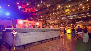An indoor venue with a bar area, wooden flooring, and exposed ceiling with lighting fixtures.