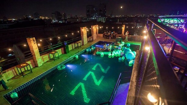 A rooftop pool with a cityscape view, surrounded by outdoor seating and illuminated by ambient lighting.