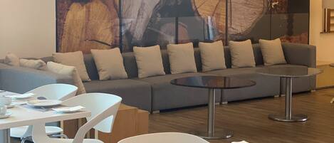 A modern lounge area with a large abstract painting, a grey sofa, and white chairs.