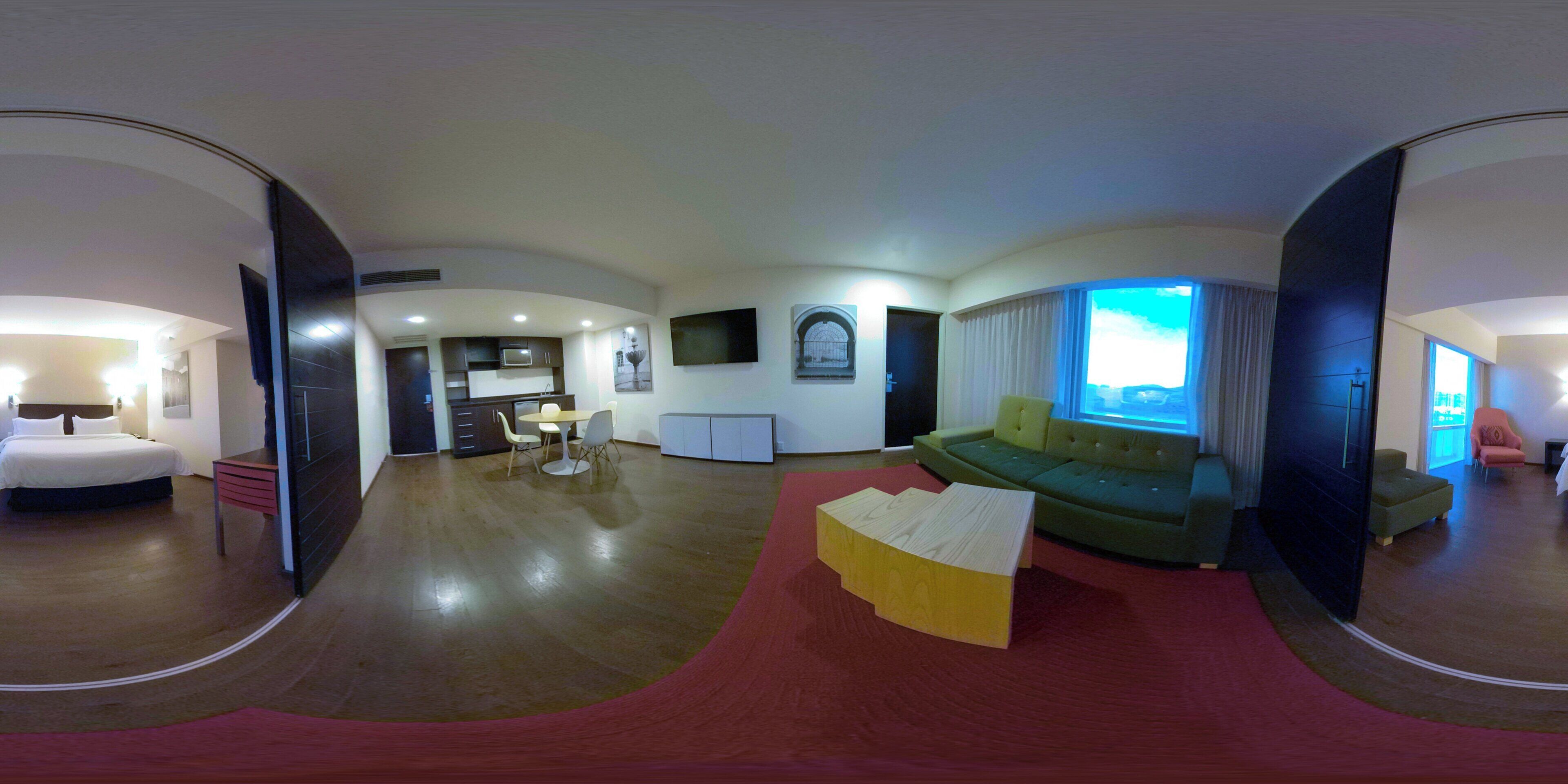 Een moderne hotelkamer met een groot bed, een zithoek, een groene bank en uitzicht op het omliggende landschap.