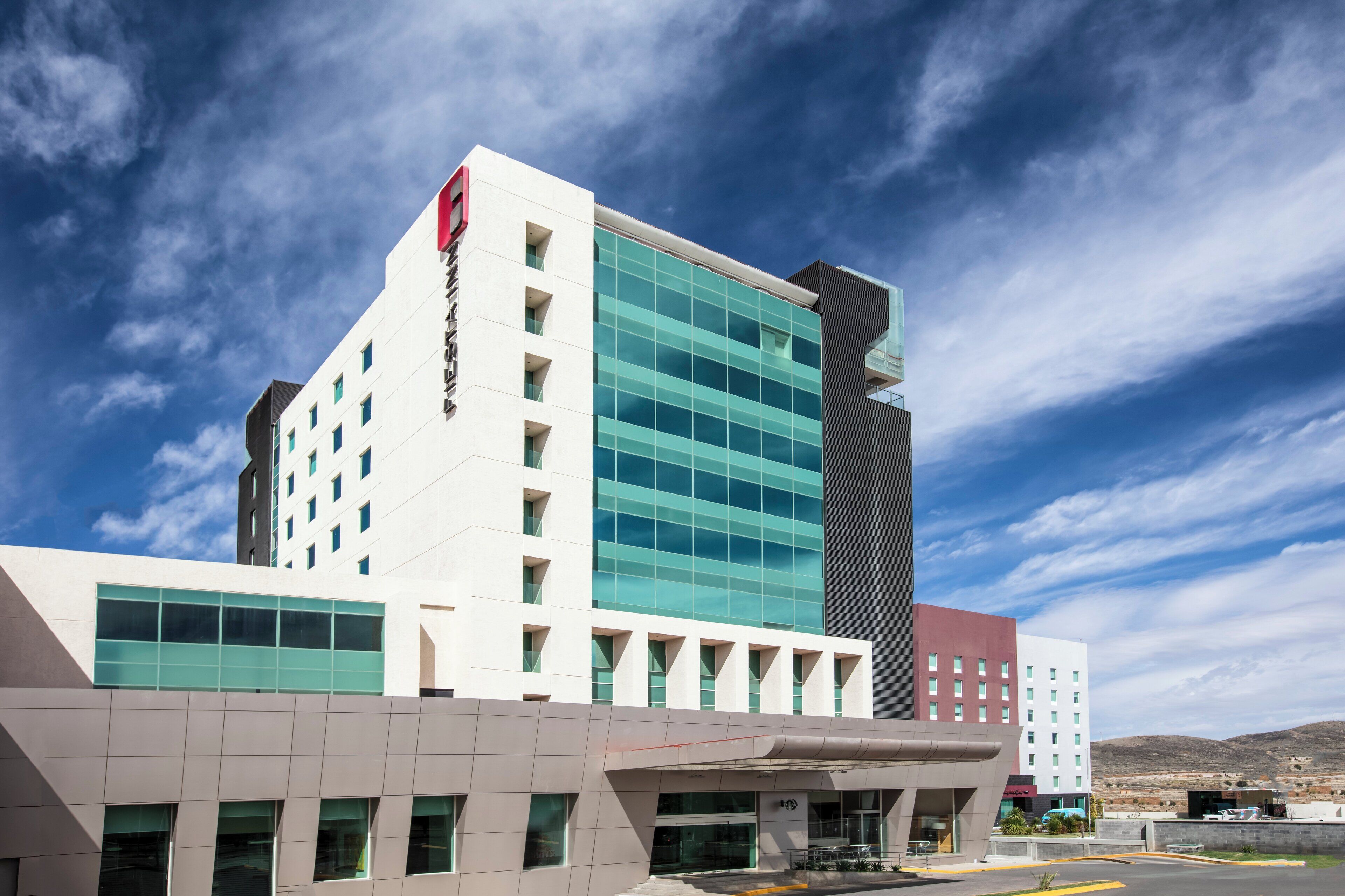 A modern hotel with a prominent glass facade, multiple floors, and a flat roof.