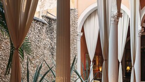 Un couloir orné de colonnes et d’arches, un palmier et un mur en pierre.