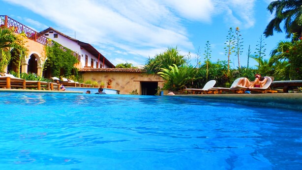 A swimming pool with lounge chairs, palm trees, and a building with a tiled roof. - Mansión de Chocolate (Granada)