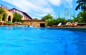 Ein Pool mit Liegestühlen, Palmen und einem Gebäude mit einem Ziegeldach.