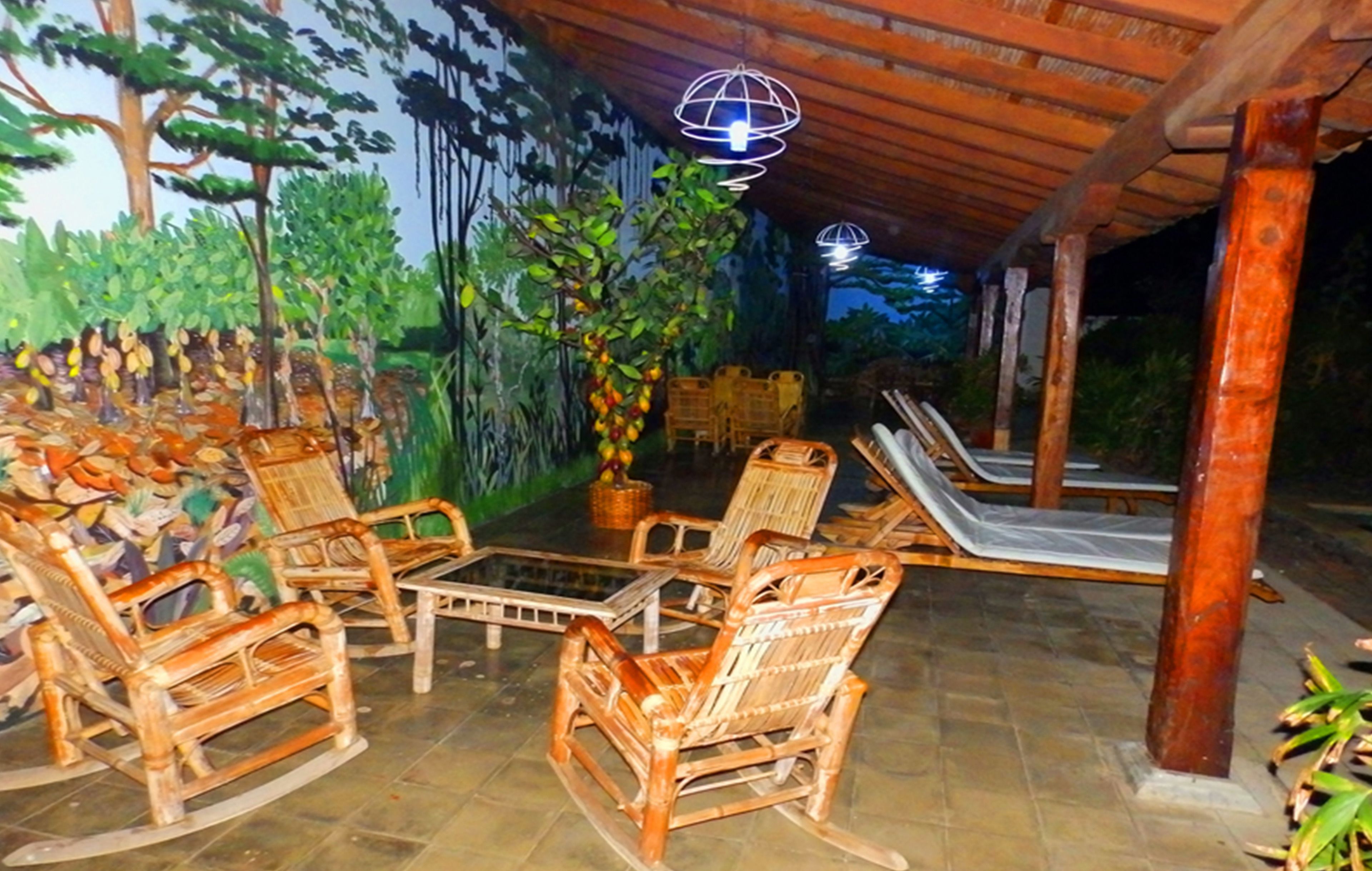 An outdoor seating area with wicker chairs and a table, surrounded by a mural of trees and plants.