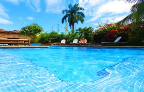 A swimming pool with clear blue water, surrounded by palm trees and lounge chairs. - Mansión de Chocolate (Granada)