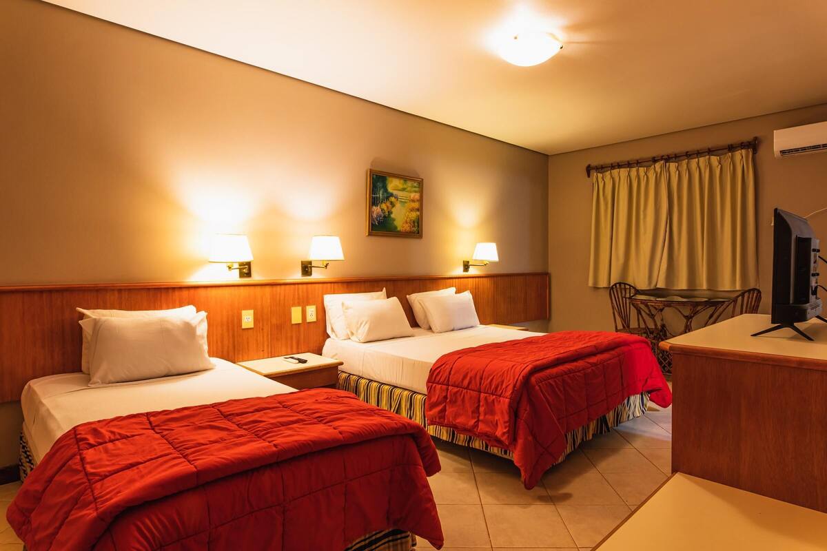 A hotel room with two beds, a desk, a chair, and a television.