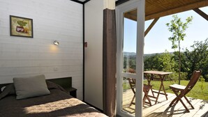 A bedroom with a bed, a pillow, a bedside table, a nightstand, a window, and a view of the outdoors.