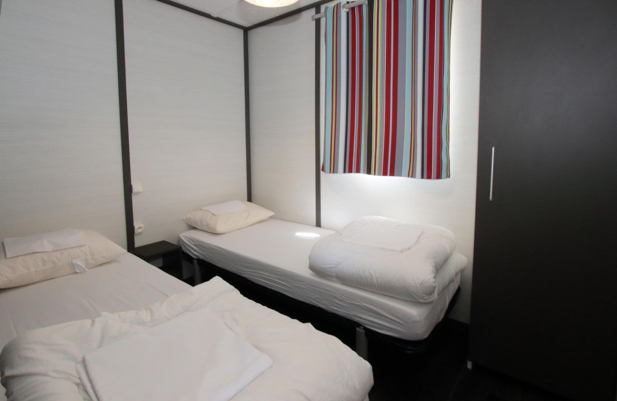 Una camera d'albergo piccola con un letto matrimoniale, un armadio scuro e una tenda a righe.