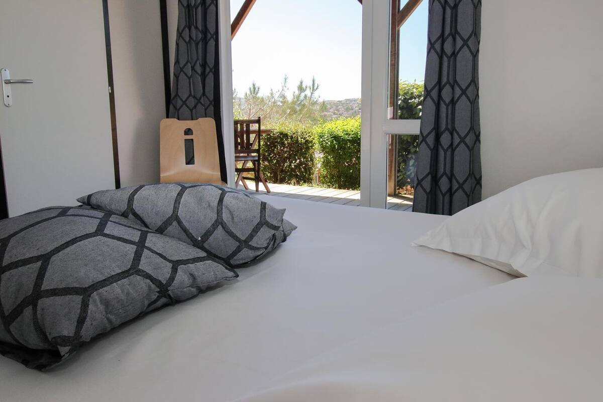 A bedroom with a bed, pillows, a guitar, and a view of the outdoors.