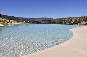 Una piscina cristalina con borde arenoso, rodeada de una zona ajardinada con sillones amarillos.