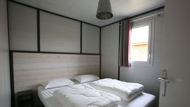 A bedroom with two beds, a wooden headboard, a window with striped curtains, and a ceiling light fixture. - Domaine de Saint Estève (Millau)
