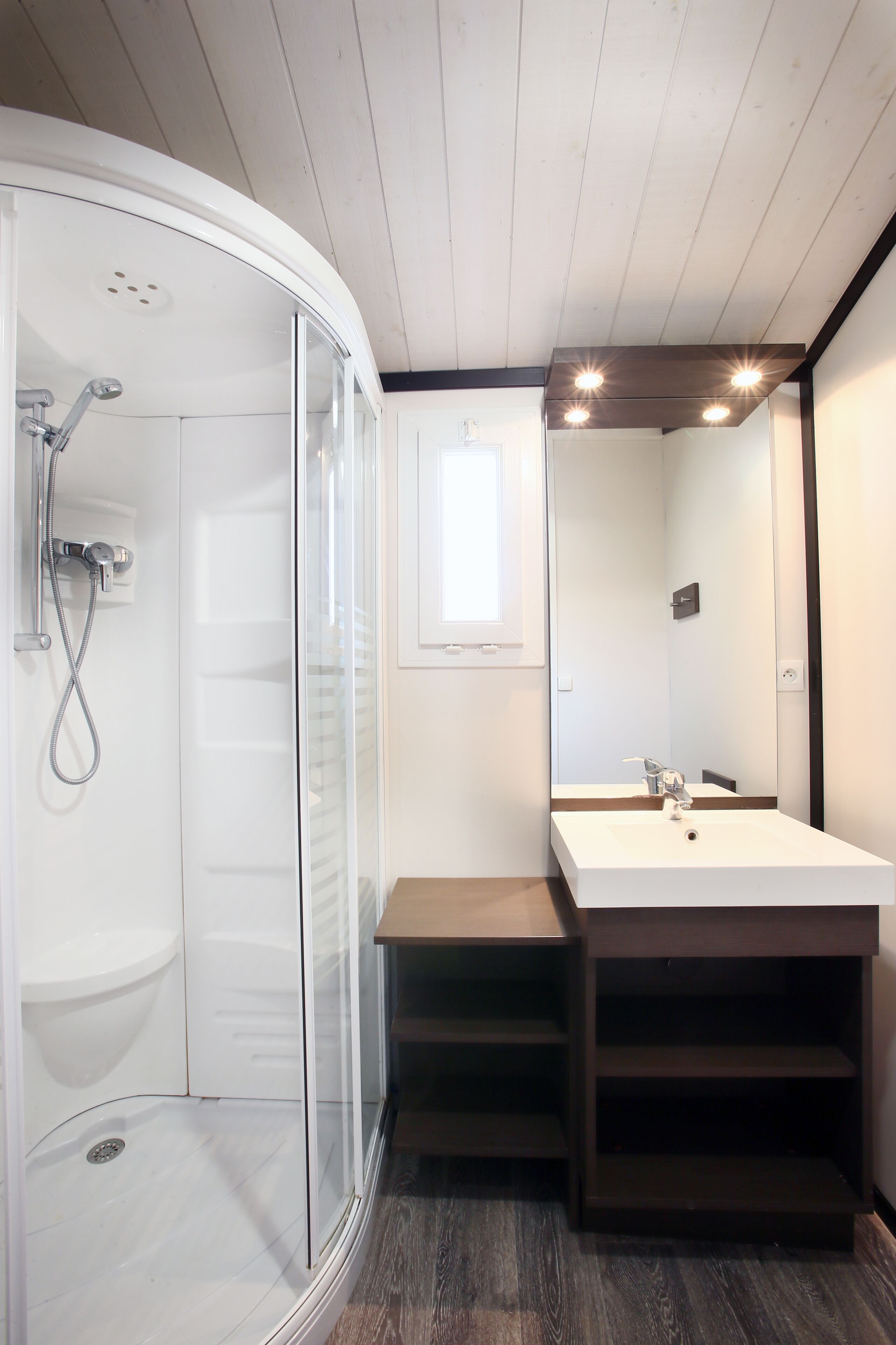 Een moderne badkamer met een glazen douchecabine, een grote spiegel en een houten wastafelmeubel.