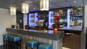 Een bar met een toonbank, krukken en flessenkast vol drank.