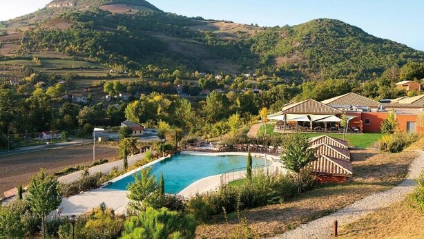 A resort with a swimming pool, outdoor seating, and a view of a mountain.