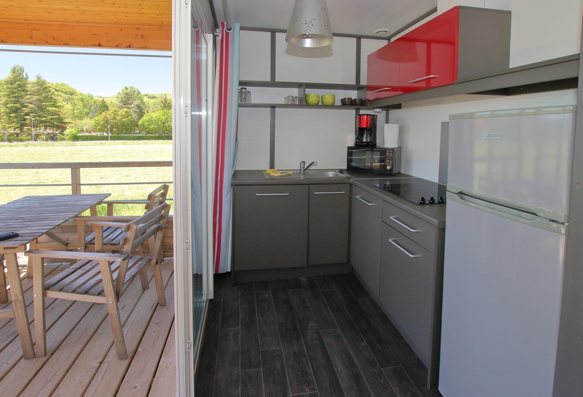 Une cuisine compacte avec des meubles gris, un meuble supérieur rouge, un four à micro-ondes et un réfrigérateur.