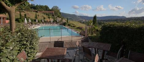 A pool area with wooden deck seating and a view of the landscape.