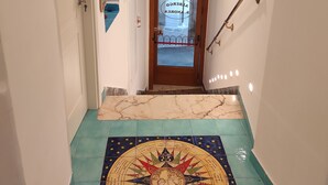 Um corredor com piso ladrilhado apresentando um desenho de bússola, uma porta de madeira com painel de vidro e um corrimão de metal.