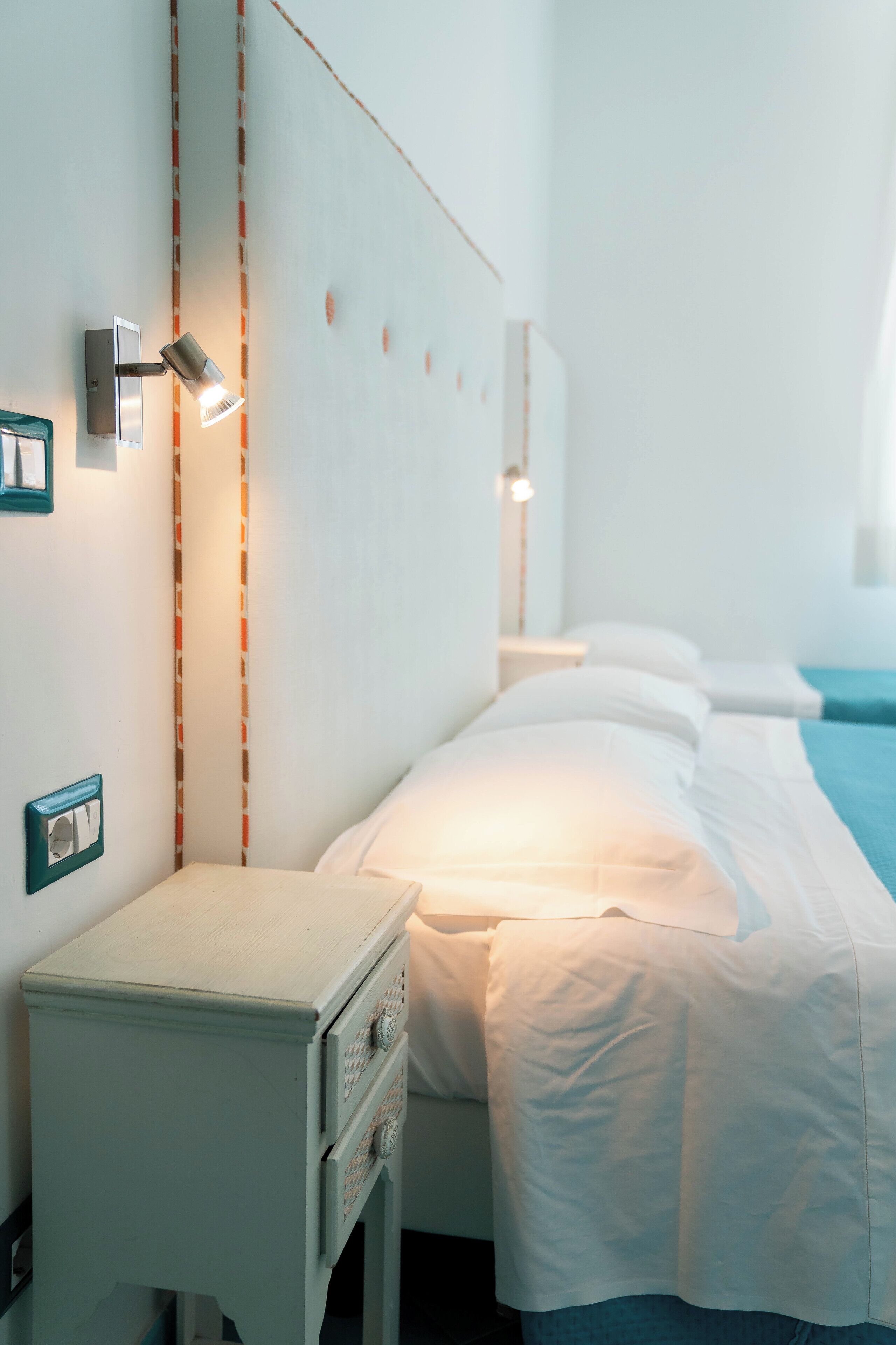 A hotel room with a bed, bedside table, and a wall-mounted light fixture.