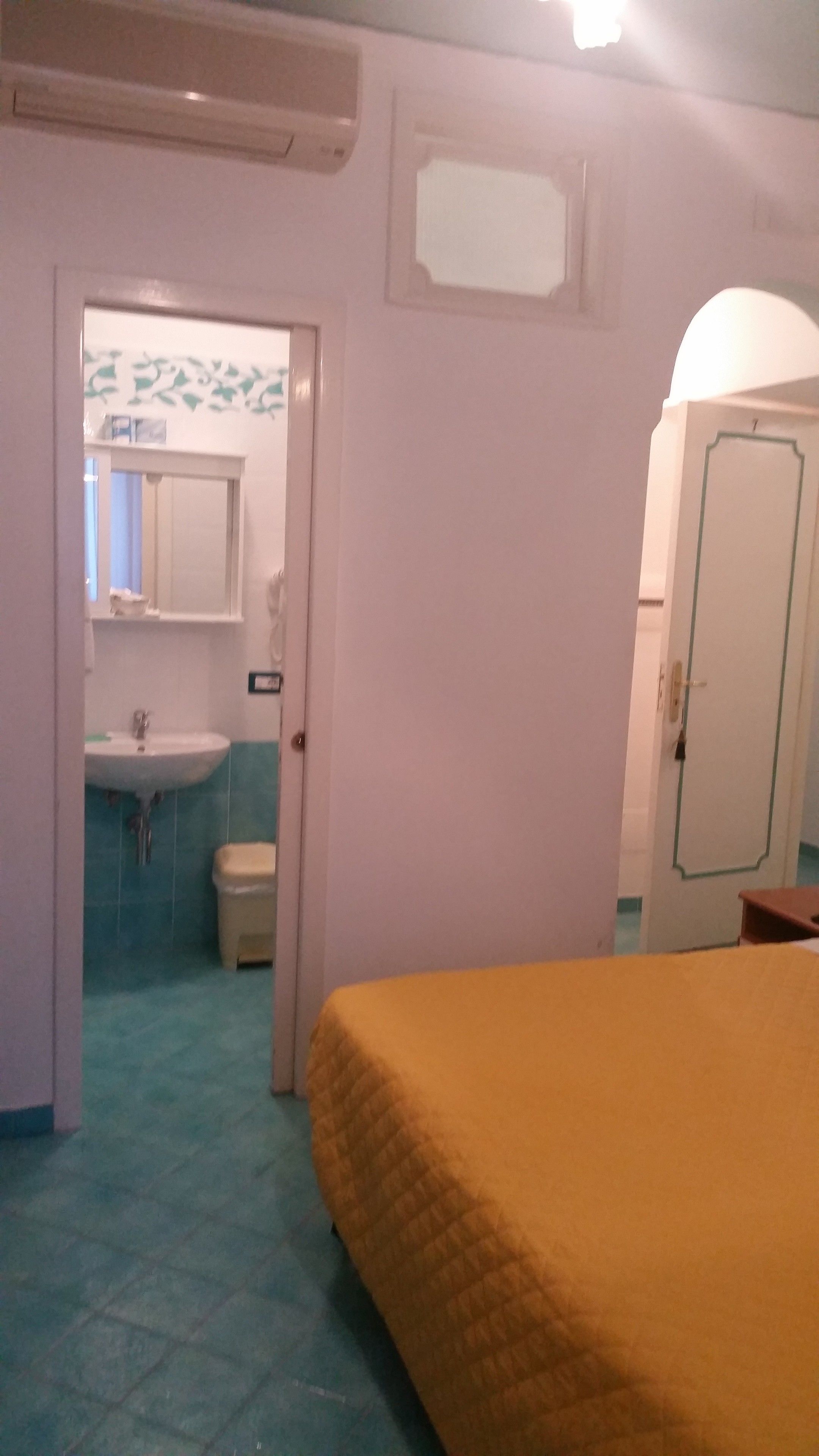 Ein Zimmer mit einem Bett, einem Badezimmer mit Waschbecken und Toilette sowie einer Tür.