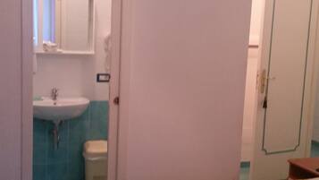 Ein Zimmer mit einem Bett, einem Badezimmer mit Waschbecken und Toilette sowie einer Tür.