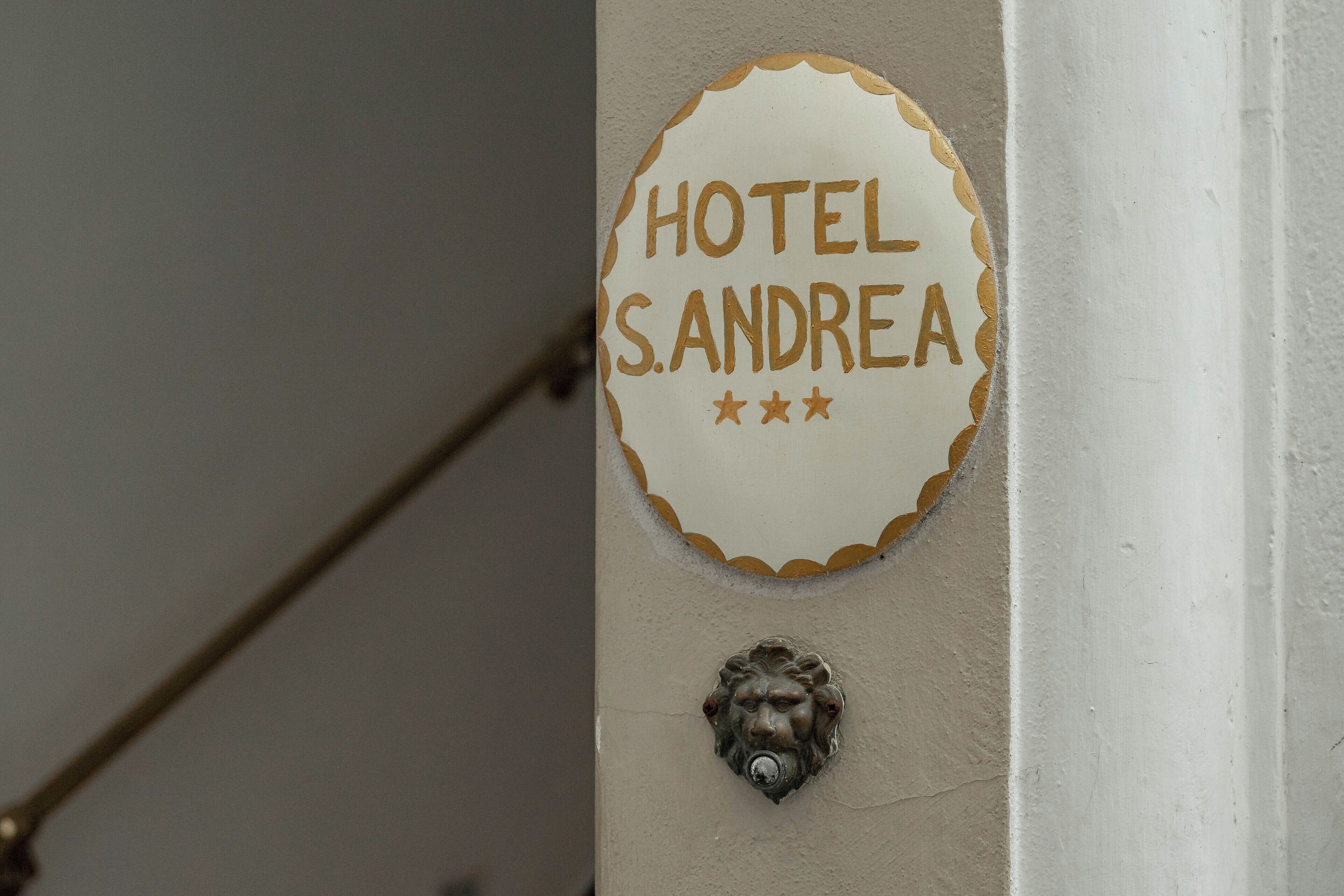 Una pared con un letrero que dice "HOTEL S. ANDREA" y un aldabón con forma de cabeza de león.